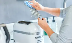 Ręce czyszczą ruszt tostera niebiesko-białą ściereczką. Dowiedz się, jak wyczyścić toster, aby był jak nowy.