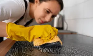Kobieta w żółtej rękawiczce czyści płytę indukcyjną gąbką z pianą. Dowiedz się, czym czyścić płytę indukcyjną, by lśniła czystością.