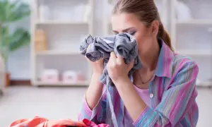 Kobieta wącha szare ubranie, szukając sposobu, jak pozbyć się zapachu stęchlizny z ubrań.