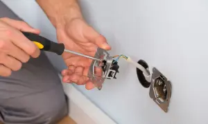 Elektryk dokonuje mostkowania gniazdka z bolcem, przykręcając mechanizm śrubokrętem. Widać przewody elektryczne.