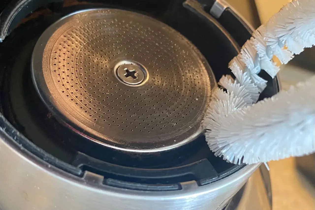 Szczoteczka czyści młynek do kawy w ekspresie DeLonghi. Drobne otwory sitka wymagają regularnego czyszczenia, by kawa była zawsze świeża.